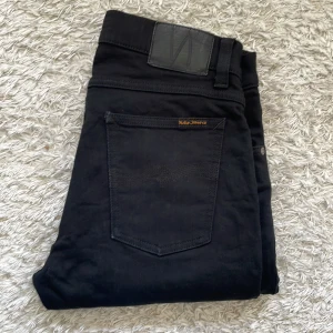 Svarta Nudie jeans - Ett par riktigt snygga svarta Nudie jeans i modellen Tight Terry! Storlek W30 L28. Använt skick 6.5/10 - lite små skavanker här och där, också nån sorts fläck på knäet som syns på sista bilden. Fråga på vid minsta fråga eller fundering🤔Priset är inte hugget i sten så kom gärna med förslag!