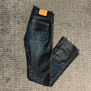 Mörkblå jeans från Nudie Jeans - Snygga mörkblå jeans från Nudie med snygga slitningar bak och fram. Jeansen har ett lite glansigare material vilket ja diggar rejält.