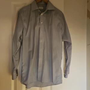 Grå skjorta från Eton, storlek 40 - Snygg grå skjorta från Eton i klassisk modell med lång ärm och knappar framtill. Skjortan har en diskret rutig struktur och är tillverkad i bomull. Perfekt för dig som gillar stilrena och tidlösa plagg.