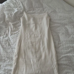 Vit kort klänning från Dilvin - Supersnygg vit kort klänning från Dilvin med smala axelband och figurnära passform. Klänningen har en enkel och stilren design som ger en fräsch vibe, perfekt för varma dagar. Materialet känns mjukt och stretchigt, vilket gör den bekväm att bära hela dagen.