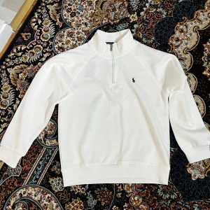 Polo tröja - Vit långärmad tröja från Polo Ralph Lauren med half zip och klassisk broderad logga på bröstet. Tröjan har hög krage och är tillverkad i mjuk bomull. Perfekt för en clean och stilren look. Har en M och S
