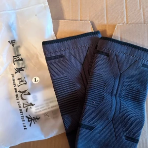 Svarta armbågsskydd storlek L - Ett par svarta armbågsskydd med tekniskt mönster och elastisk passform. Perfekta för träning och ger extra stöd runt armbågen. Materialet är syntetiskt och andas bra, vilket gör dem bekväma under intensiva aktiviteter.