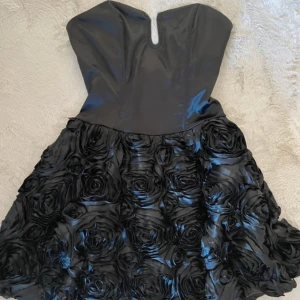 Klänning med rosor - Galet fin klänning! Svart korsettliknande ”satin” byst tillsammans med en vacker kjol full med rosor i tyg. Dragkedja på sidan finns på sida.  Obs. Liten spricka i en ros vid midjan, se bild. Storlek 8 motsvarar S / 36.  Prissatt för 920kr via Vestiaire. 