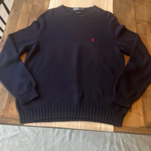 Stickad kofta Ralph Lauren - Mörkblå stickad tröja från Polo Ralph Lauren i 100% bomull. Klassisk modell med rund hals, ribbade muddar och röd broderad logga på bröstet. Perfekt för lager-på-lager och snygg till jeans eller chinos. Storlek L men passar XL. Vid frågor är det bara att ställa👍