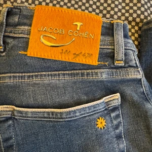 Jacob Cohën Limited Edition jeans blå - Blå jeans från Jacob Cohën, Limited Edition Style 622. Klassisk femficksmodell med snygga kontrastsömmar, läderpatch bak och unika detaljer som broderad blomma på bakfickan. Knappar med logga och italienska flaggdetaljer. Raka ben och normal passform. Bara provat på dom inte använt. (NY)