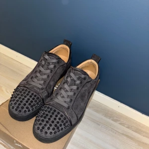 Christian Louboutin Louis Strass sneakers - Säljer ett par gråa Christian Louboutin i mocka med gråa spikar på tån och klassisk röd sula. Skorna har snörning och en lyxig känsla med unika detaljer. Perfekta för dig som vill sticka ut med din stil.