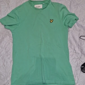 Grön t-shirt från Lyle & Scott - Snygg grön t-shirt från Lyle & Scott med klassisk passform och korta ärmar. T-shirten har en liten gul logga på bröstet och är tillverkad i mjuk bomull. Perfekt för en avslappnad och stilren look.