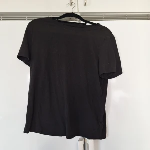 Svart basic t-shirt i bomull M - Enkel svart t-shirt med rund hals och korta ärmar. Tillverkad i mjuk bomull och har en klassisk passform som funkar till det mesta. Perfekt för dig som gillar stilrena och bekväma plagg.