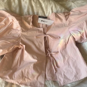 Ljusrosa blus med puffärmar Gina Tricot - Aldrig använt!!!Supersöt ljusrosa blus från Gina Tricot med stora puffärmar och två knytband framtill. Blusen har en rak passform och är tillverkad i ett slätt bomullstyg. Perfekt för dig som gillar romantiska och trendiga detaljer.