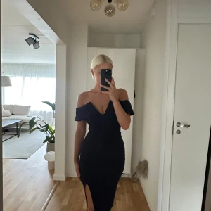 Marinblå offshoulder långklänning - Säljer en marinblå långklänning med offshoulder och v-ringad urringning. Klänningen har en snygg slits framtill och figurnära passform som framhäver siluetten. Materialet är mjukt och stretchigt polyester. Perfekt för dig som vill sticka ut.