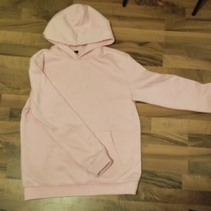 Ljusrosa hoodie med björnmotiv - Säljer en ljusrosa hoodie med stor svartvit björnprint på ryggen. Tröjan har huva, lång ärm och en klassisk magficka framtill. Perfekt för dig som gillar streetstyle och vill sticka ut med ett coolt motiv.