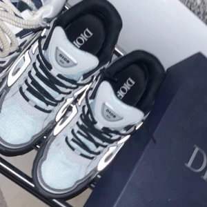  sneakers i vitt och svart - Säljer ett par  B22 sneakers med vit mesh, svarta och grå detaljer samt reflekterande partier. Skorna har svart sula, svarta snören och tydlig logga på plösen och innersulan. Riktigt snygga och trendiga sneakers som sticker ut.