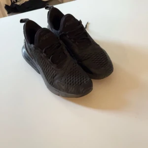Svarta Nike Air Max 270 sneakers - Säljer ett par helsvarta Nike Air Max 270 sneakers med mesh-ovandel och synlig Air-enhet i hälen. Skorna har snörning, rund tå och sportig vibe. Perfekta för dig som gillar streetstyle och vill ha bekväma skor med snygg design. Trasiga me ett hål som nu ser på sista bilden därför priset