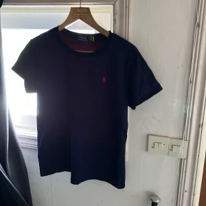 Mörkblå t-shirt Polo Ralph Lauren M-S - Snygg mörkblå t-shirt från Polo Ralph Lauren i storlek M men känns mer som en S. Klassisk passform med korta ärmar och rund hals. Ikoniska röda loggan broderad på bröstet. Tillverkad i mjuk bomull som känns skön mot huden. 