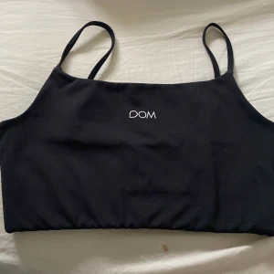 Svart linnetopp från Drop of Mindfulness - Svart linnetopp med smala, justerbara axelband och vit logotyp både fram och bak. Toppen är croppad och har en bred resår nedtill för extra stöd. Perfekt för träning eller chill dagar. Materialet är mjukt och stretchigt syntet.