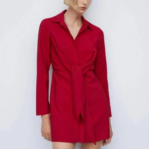 skjortklänning med knyt från Mango - Säljer en röd skjortklänning från Mango i kort modell. Klänningen har långa ärmar, klassisk krage och snygg knytning framtill som ger en cool twist. Perfekt för dig som gillar stilrena men ändå trendiga plagg.