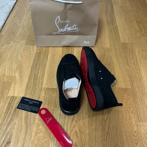 Christian Louboutin suede - Snygga svarta sneakers från Christian Louboutin med klassisk röd sula och diskret logga undertill. Skorna har rund tå, snörning och är tillverkade i mocka med läderdetaljer. Perfekta för dig som vill sticka ut med exklusiv stil och ikoniska detaljer. PASSAR 43,5
