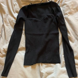 Svart ribbad långärmad topp - Snygg svart ribbad topp med lång ärm och en unik sweetheart-urringning. Toppen är figurnära och har en stilren look som passar till många outfits. Perfekt för dig som gillar minimalistisk stil med en twist.