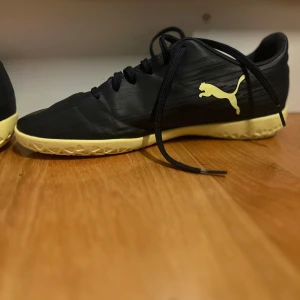 Svarta och gula Puma fotbollsskor - Säljer ett par snygga svarta Puma fotbollsskor med gula detaljer och sula. (Det är futsal skor).
