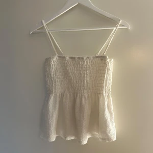 Vit smockad linnetopp med volang - Supersöt vit linnetopp med smockad överdel och tunna axelband. Det gråa där uppe är bara skugga (kan ses på andra bilden). Mycket bra skick! 