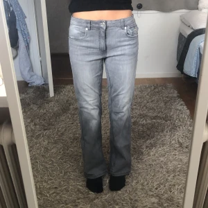 Grå bootcut jeans från Kappahl - Snygga grå jeans från Kappahl i bootcut-modell med låg midja. Jeansen har klassiska fem fickor, coola detaljer på bakfickorna med knappar och är tillverkade i ett mjukt jeanstyg. Perfekta för dig som gillar en avslappnad men trendig look.