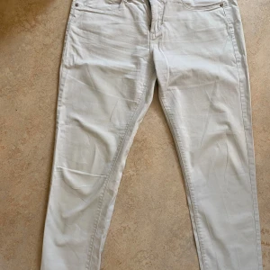 Beiga chinos från KappAhl, stl 40 - Snygga beiga chinos från KappAhl i storlek 40. Klassisk femficksmodell med dragkedja och knapp framtill. Byxorna har raka ben och är tillverkade i mjuk bomull, perfekta för en clean och stilren look.