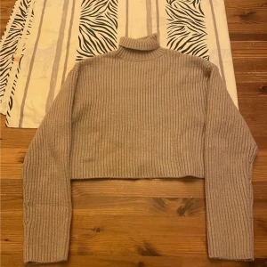 Beige croppad polotröja från H&M - Ribbstickad beige polotröja från H&M i croppad modell. Tröjan har lång ärm och hög krage, perfekt för lager-på-lager. Mjuk och skön, passar till både jeans och kjol för en chill look.