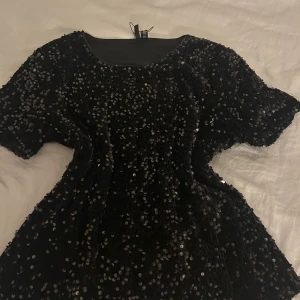 Svart paljettopp från H&M - Säljer en svart topp från H&M som är täckt med glittrande paljetter. Toppen har rund halsringning och korta ärmar, perfekt för att sticka ut. Materialet är mjukt och följsamt med en snygg glansig finish.