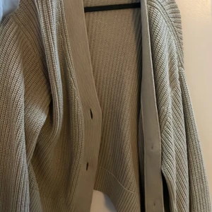 Beige stickad kofta från H&M - Säljer en beige stickad kofta från H&M i storlek M. Koftan har grovstickad struktur, djup v-ringning och stora knappar framtill. Perfekt för lager-på-lager och chill vibes. Passar dig som gillar en enkel men snygg look.