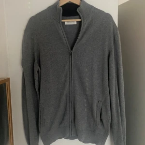 Grå kofta med dragkedja från Pier One - Snygg grå kofta från Pier One med hel dragkedja framtill och ribbad krage. Tröjan har långa ärmar och två fickor på sidorna. Perfekt för dig som gillar enkel och stilren design. Materialet är mjukt och känns skönt mot huden. Kom dm för fler frågor eller bilder. Kan gå ner pris vid snabb affär. 