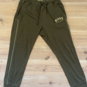 Mjukisbyxor från Hugo Boss - Mjukisbyxor från Hugo Boss med broderad logga på vänster sida. Byxorna har snörning i midjan, ribbade muddar vid bensluten och diskreta ränder längs sidorna. Tillverkade i mjuk bomull för maximal komfort och avslappnad stil.