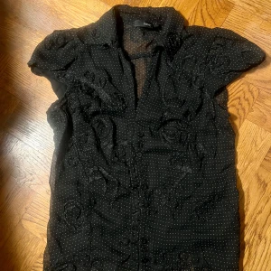 Svart prickig blus från Next - Svart  blus från Next med små vita prickar och broderade blommor. Korta puffärmar, klassisk krage och knäppning framtill😍