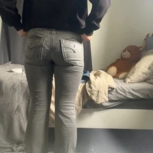 Grå bootcut jeans från Gina Tricot - Snygga grå jeans från Gina Tricot i bootcut-modell. Jeansen har klassiska fickor både fram och bak, med coola detaljer på bakfickorna. De är tillverkade i ett mjukt jeanstyg och har en bekväm passform med normal midja.