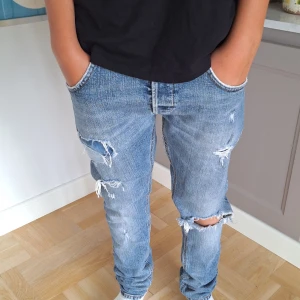 Blå slitna jeans med raka ben - Snygga blå dondup jeans med slitningar och hål på knä och lår. Raka ben och klassisk femficksmodell. Jeansen har orange sömmar på bakfickorna och är tillverkade i mjukt denimtyg. Perfekta för en avslappnad streetstil.