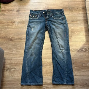 True Religion Joey bootcut jeans - Säljer ett par blå True Religion Joey jeans med bootcut passform. Coola slitningar framtill och stora bakfickor med truey hästsko.