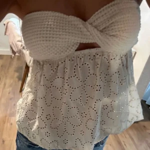 Vit broderad bandeau tubtopp - Supersöt vit bandeau tubtopp med virkad twistad överdel och broderade blommor i tyget nedtill. Toppen är ärmlös och har en luftig, somrig känsla. Perfekt till jeans eller kjol för en fräsch look.