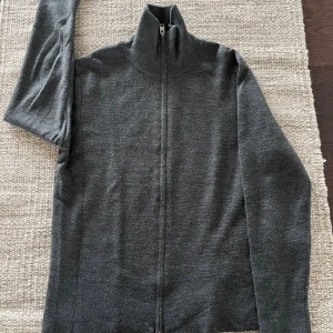 Mörkgrå kofta med dragkedja från H&M - Mörkgrå stickad kofta från H&M med hel dragkedja framtill och hög krage. Regular fit och långärmad modell, perfekt för lager-på-lager. Enkel och stilren design som funkar till det mesta.