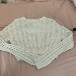 Vit kabelstickad tröja från H&M - Säljer en vit kabelstickad tröja från H&M. Tröjan har en croppad passform, ribbade muddar och lång ärm. Perfekt för lager-på-lager och har en klassisk kabelstickad struktur som ger en snygg och tidlös look.