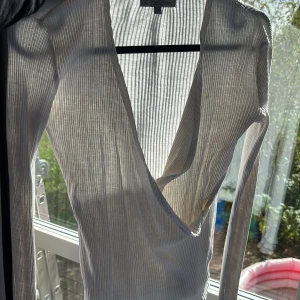 Vit omlottopp med djup v-ringning - Säljer en vit omlottopp från Sea Breeze i ribbad bomull. Toppen har lång ärm, djup v-ringning och smal passform. Perfekt för dig som gillar stilrena och enkla plagg med lite extra edge. Snygg att matcha med jeans eller kjol.