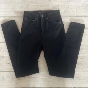Svarta jeans från Nudie Jeans, W26 L28 - Svarta jeans från Nudie Jeans med klassisk fyrficksdesign och snygga detaljer på bakfickorna. Jeansen har smal passform och är tillverkade i mjukt bomullstyg. Perfekta för dig som gillar stilrena och tidlösa byxor. Jeansen är i väldigtbra skick. W26 L28 säljs för 400kr, kontakta om frågor 