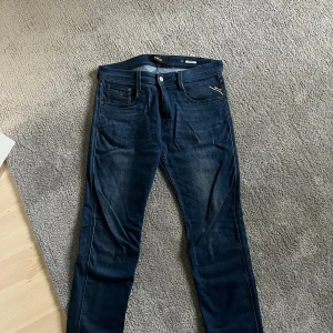 Replay Anbass jeans mörkblå - Snygga mörkblå Replay Anbass jeans med klassisk femficksdesign och läderpatch bak. Jeansen har en smal passform och är gjorda i stretchig bomullsdenim för extra komfort. Perfekta för dig som gillar en modern och stilren look. W31 L32, 31/32