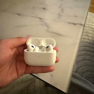 AirPods Pro 2 - Apple AirPods Pro med laddningsetui. Trådlösa hörlurar med aktiv brusreducering och silikonproppar för bästa passform. Skicket är begagnat med synligt slitage och mindre repor på etuiet, men fungerar som de ska.