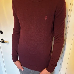 Vinröd merinoullströja Polo Ralph Lauren - Säljer en vinröd långärmad tröja från Polo Ralph Lauren i slim fit. Tröjan är tillverkad i mjuk och tvättbar merinoull och har en broderad logga på bröstet. Perfekt för dig som gillar klassisk och stilren look. Bra skick använd ett fåtal gånger. Pris kan diskuteras