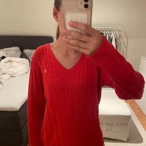 Röd kabelstickad tröja Ralph Lauren - Säljer en röd kabelstickad tröja från Ralph Lauren med v-ringning och lång ärm. Tröjan är i 100% bomull och har en klassisk, tidlös look med diskret logga på bröstet. Perfekt för dig som gillar preppy stil och vill ha något snyggt och bekvämt. Skulle säga att den är mer i storlek M.