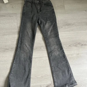 Grå bootcut jeans med hög midja - Snygga grå jeans med bootcut och hög midja. Jeansen har klassisk femficksdesign, dragkedja och knapp framtill. Materialet är denim med en tvättad look. Spärattade ben där nere och trasig grej upp vid magen.