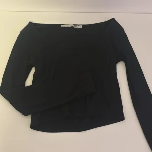 Svart ribbad långärmad topp 157 - Svart långärmad topp från 157 med ribbad struktur och croppad passform. Toppen har en bred, rundad urringning och är tillverkad i ett mjukt, stretchigt material som sitter snyggt på kroppen. Perfekt att styla med jeans eller kjol.