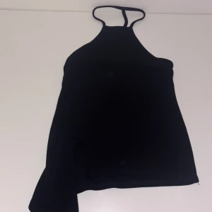 Svart asymmetrisk halterneck topp Boohoo - Säljer en svart halterneck topp från Boohoo i storlek 34. Toppen har smala axelband, asymmetrisk nederkant med slitsdetalj och är ärmlös. Perfekt för dig som gillar minimalistisk och trendig stil.