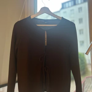 Brun omlottkofta från Gina Tricot - Aldrig använd, säljs för att den är för stor. Säljer en brun omlottkofta från Gina Tricot med långa ärmar och snygga knytband framtill. Koftan har en enkel, stilren design och är perfekt att styla med jeans eller kjol. Materialet känns mjukt och lätt, och färgen är djup chokladbrun. 🥰🥰