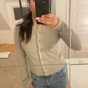 Beige kofta från H&M med knappar - Säljer en beige kofta från H&M i storlek S. Koftan har rund hals, långa ärmar och knappar hela vägen framtill. Materialet är mjukt och tunt, perfekt för lager-på-lager. Passformen är normal och den är enkel att matcha med jeans eller kjol.