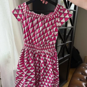 Rosa och vit kortklänning från Prada - Superfin kortklänning från Prada med rosa och vitt geometriskt mönster. dragkedja i ryggen! Detta är vintage så står tyvärr ingen storlek men skulle tippa på small! Passar perfekt för mindre barn!